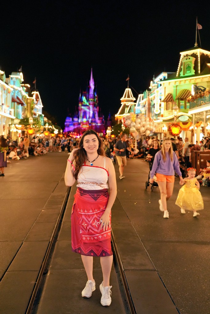 Gabriela Bordin fantasiada na Main Street do Magic Kingdom à noite, com o castelo iluminado ao fundo durante a festa de Halloween
