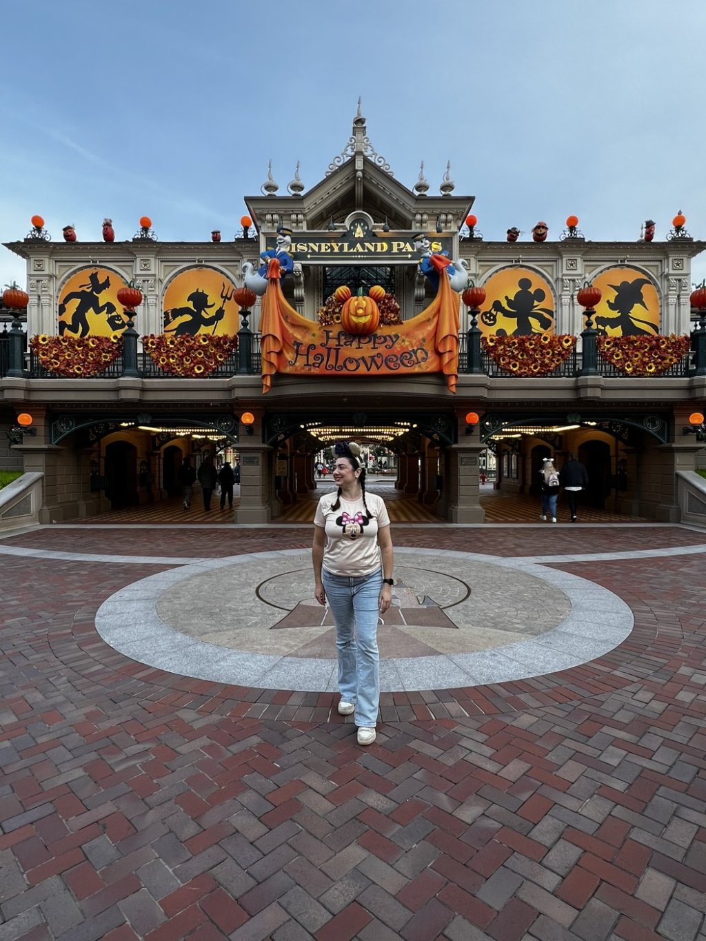 Gabriela Bordin na entrada da Disneyland Paris decorada para o Halloween, com abóboras e o letreiro Happy Halloween
